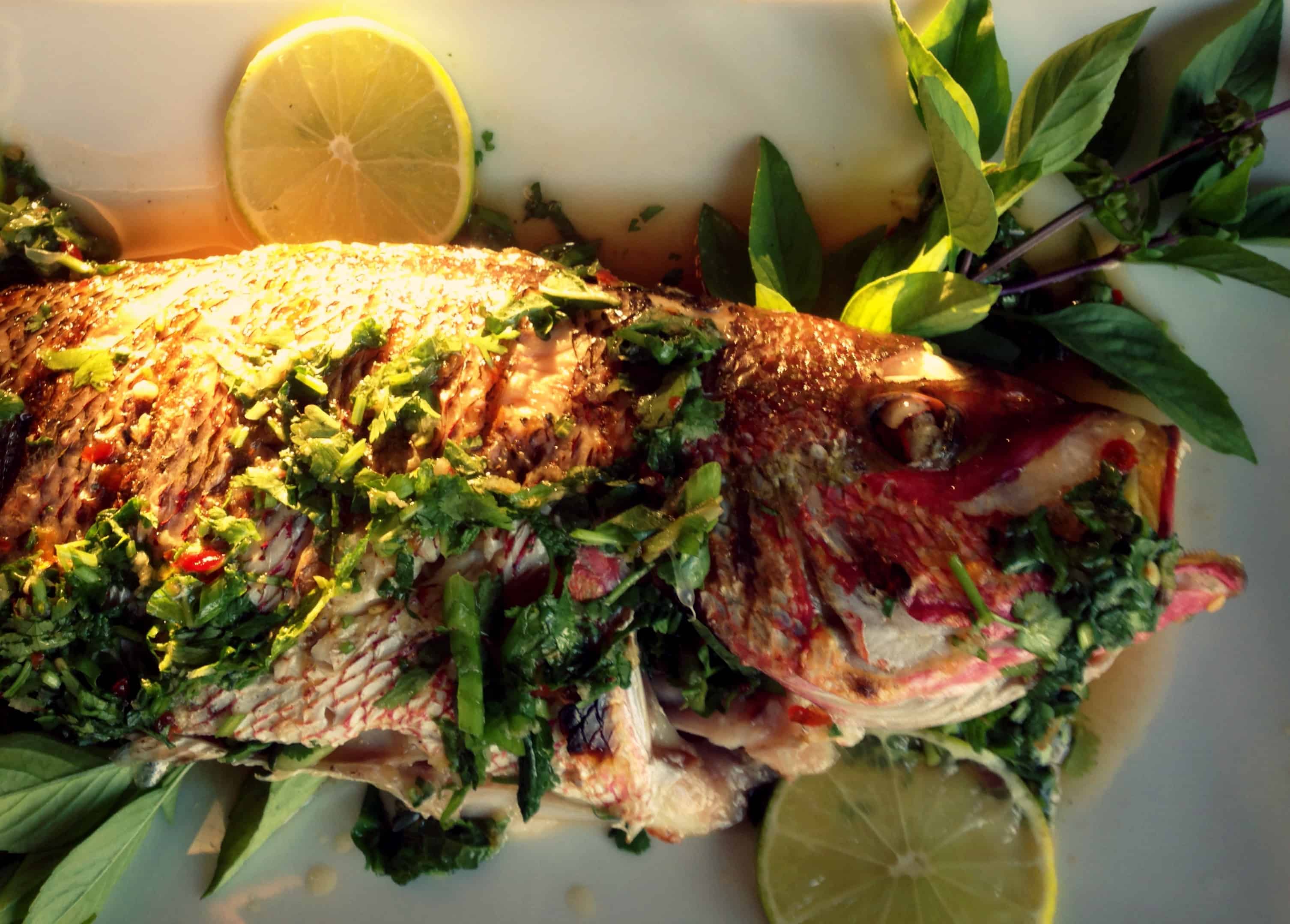 Whole grilled snapper on a platter with fresh herbs.