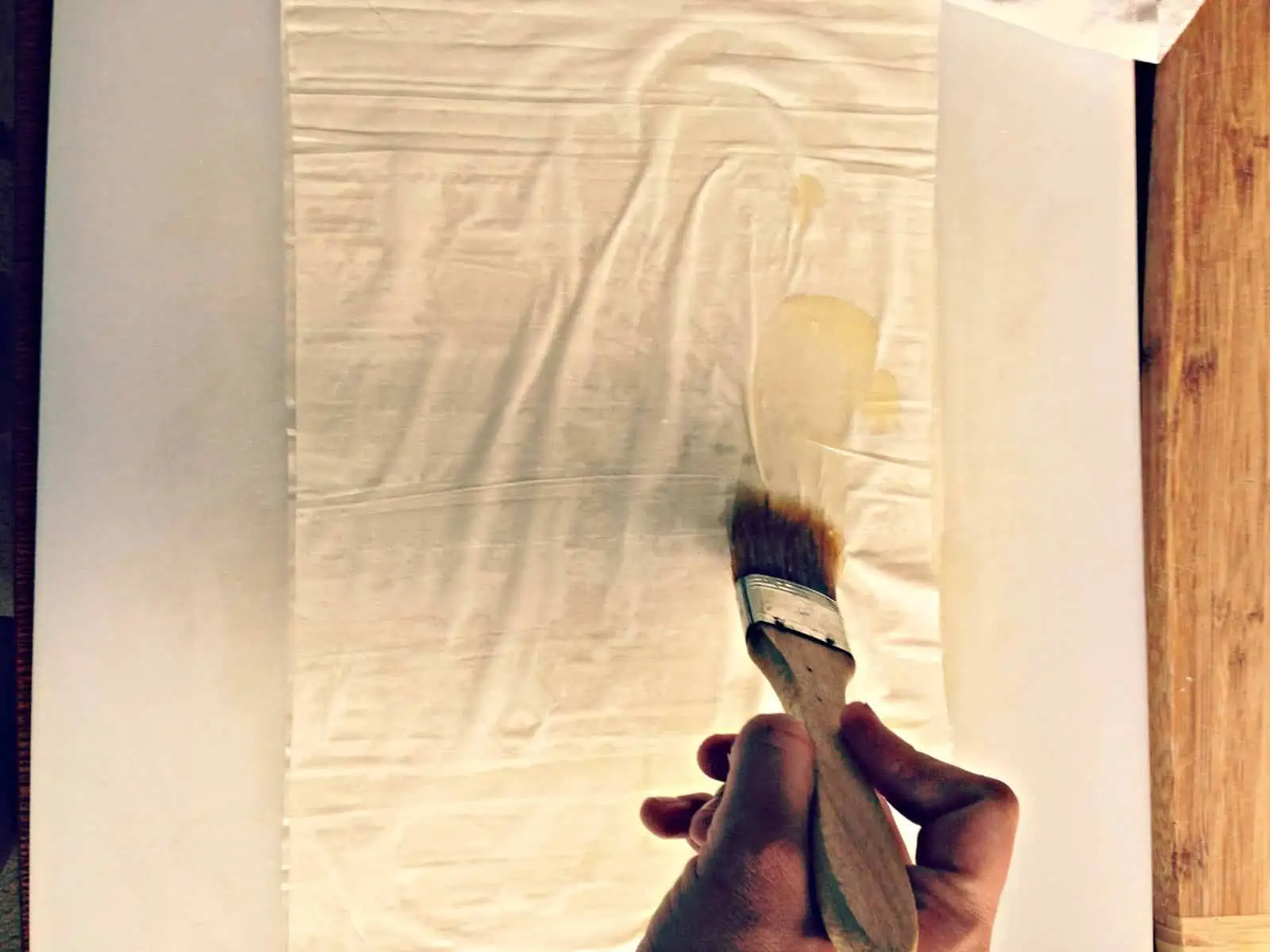 Brushing butter onto a sheet of puff pastry using a pastry brush.