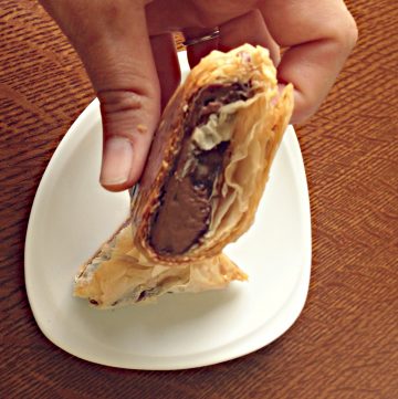 A hand holding a puff pastry filled with nutella and banana.