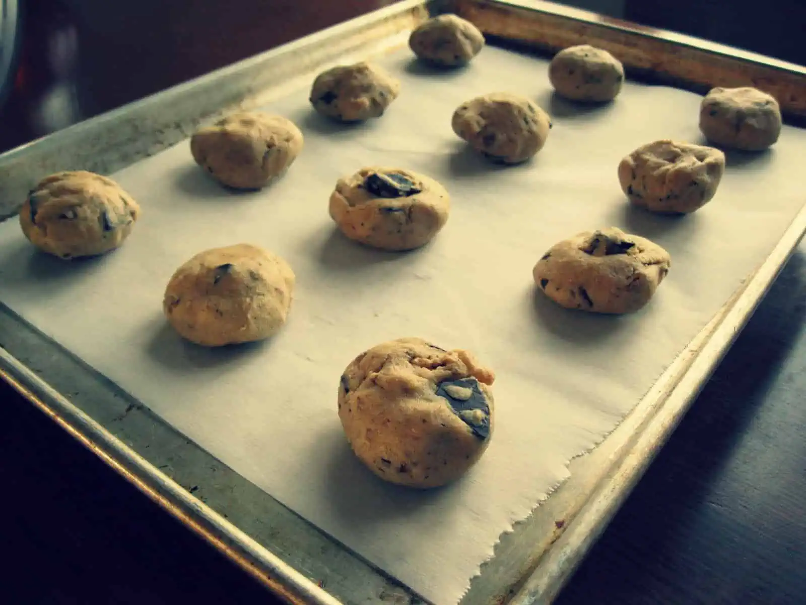 Chocolate chip cookie dough balls sitting on a parchment lined baking sheet.