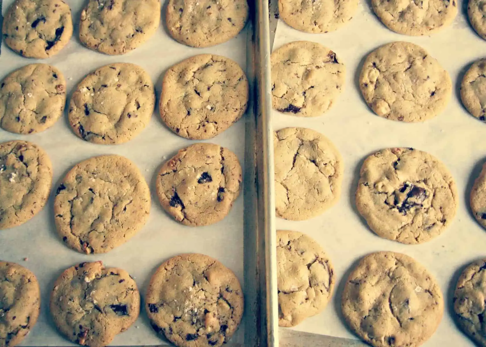 Two parchment lined baking sheets filled with baked chocolate chip cookies.