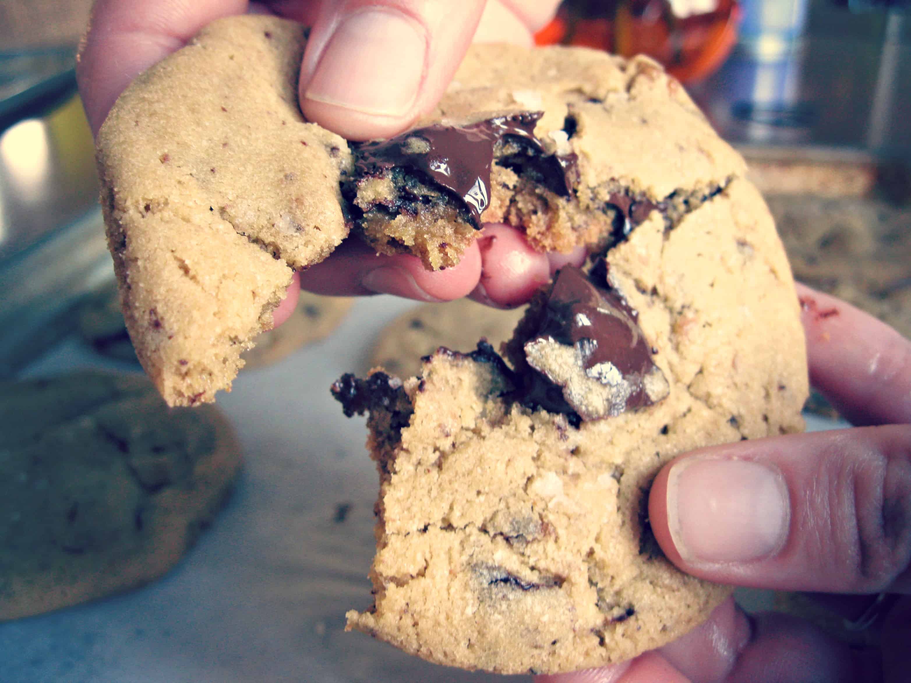 Two hands breaking a chocolate chip cookie in half.