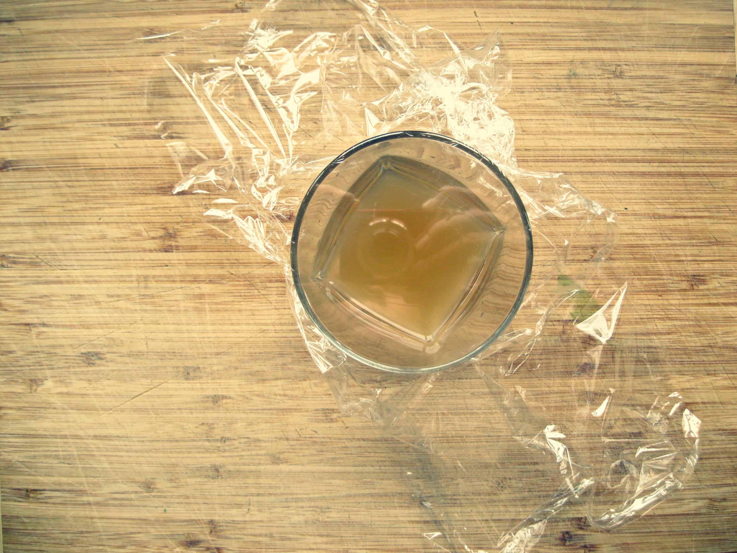 Plastic wrap overtop of a glass with apple cider vinegar.