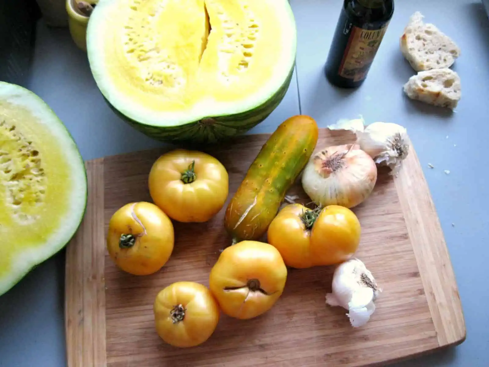 Yellow tomatoes, onions, and yellow watermelon on a cutting board.