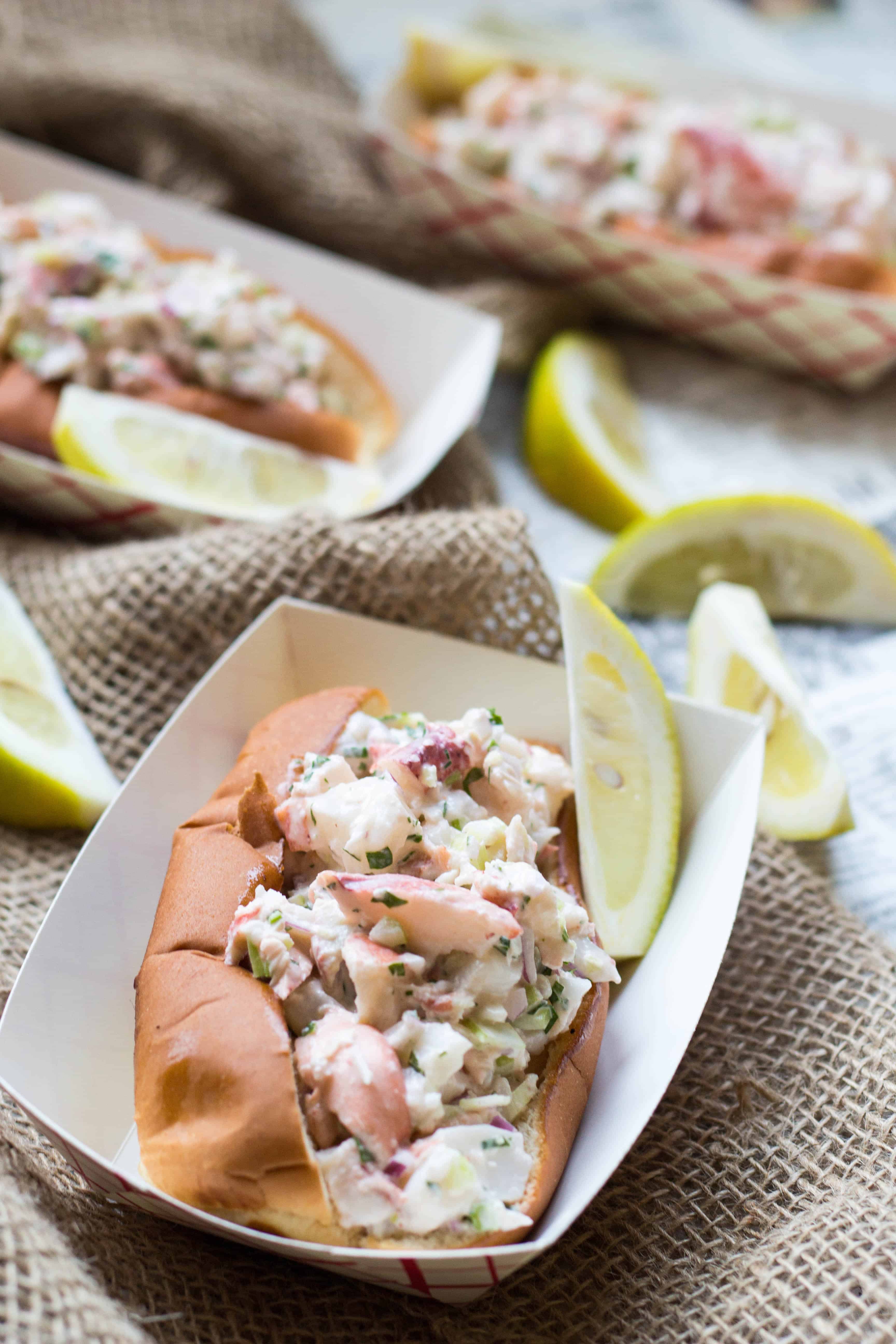 Close up of a lobster roll in a paper boat with a lemon wedge.