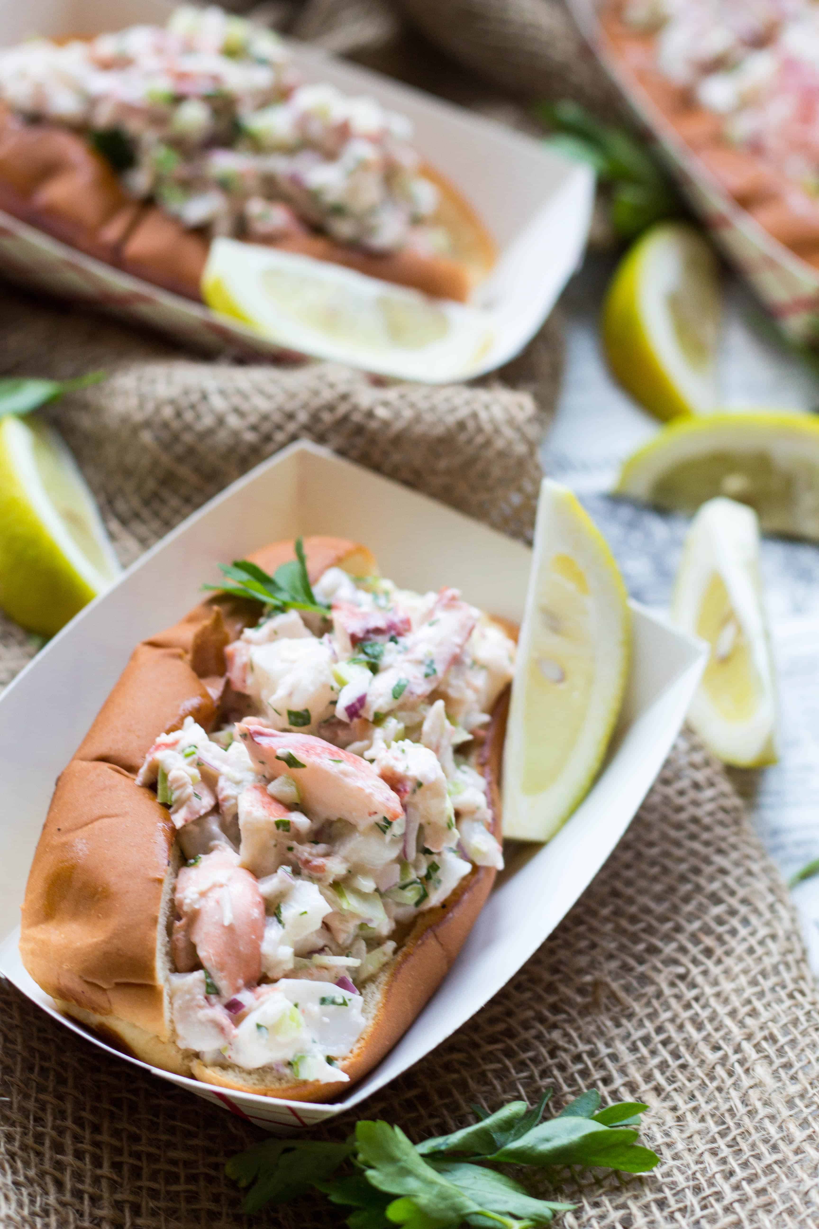 Close up of a lobster roll and lemon wedges in a paper food boat.
