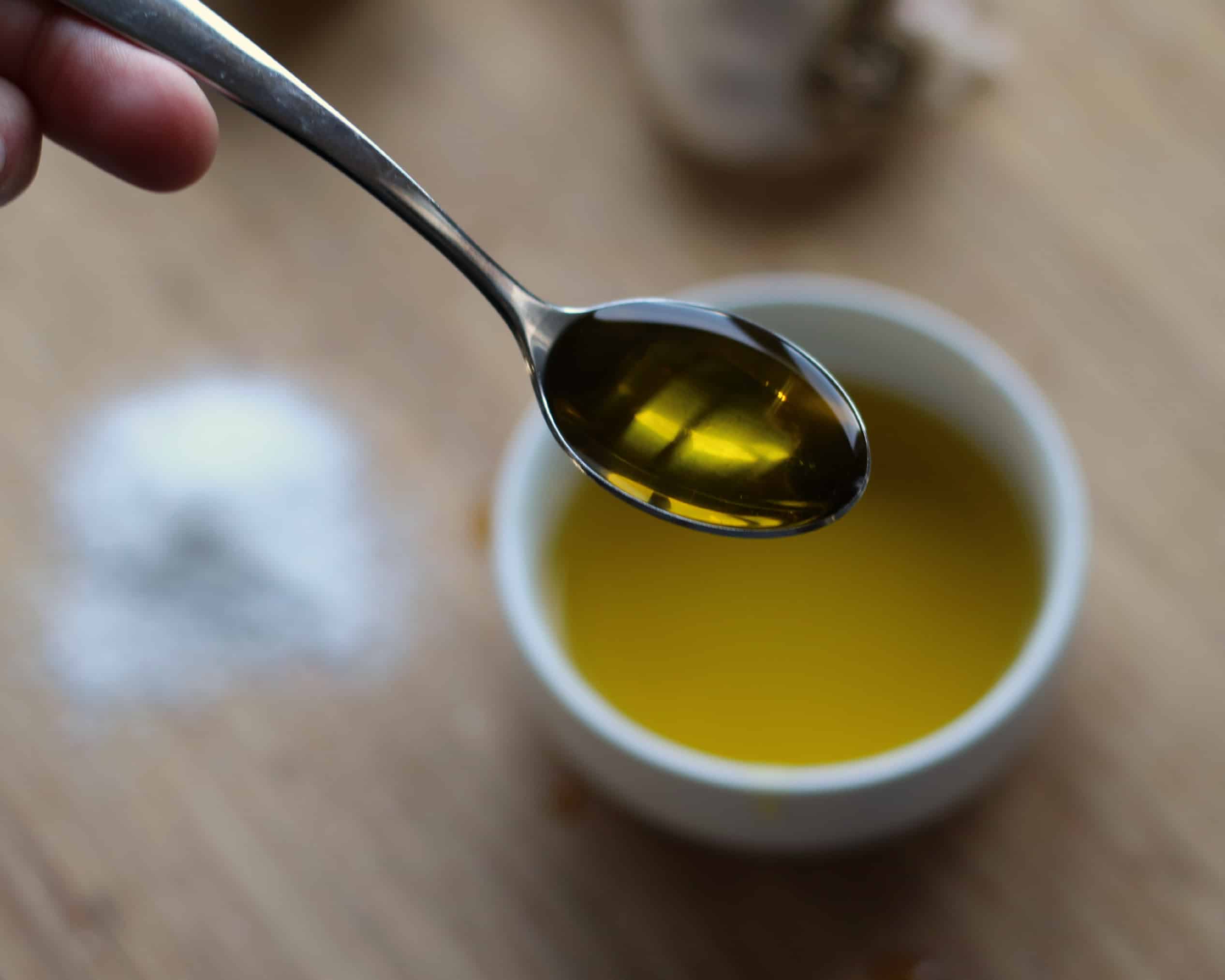 A spoonful of olive oil over a small white bowl.