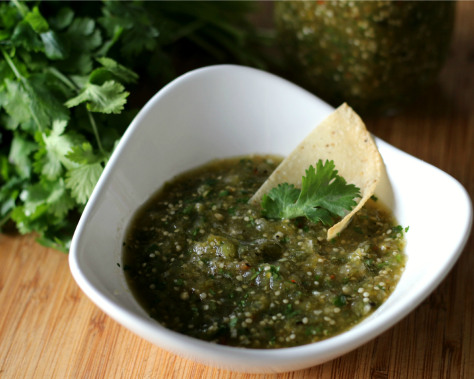 A tortilla chip in a small white bowl of salsa verde.