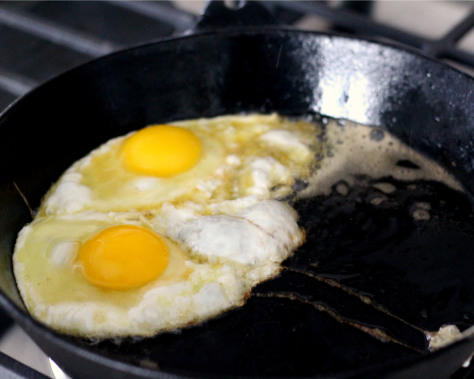 Two eggs frying in a cast iron skillet.