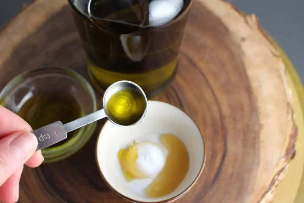 A tablespoon pouring olive oil onto an egg yolk with sugar in a small bowl.
