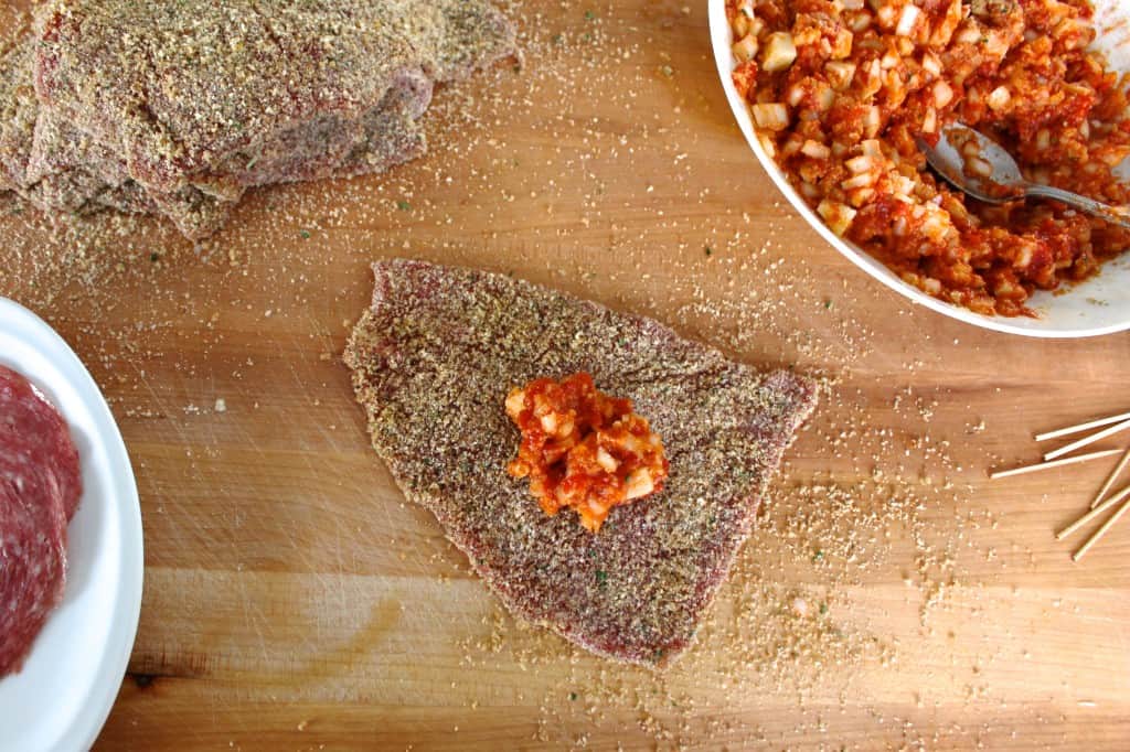 Tomato filling placed on a breaded beef steak slice on a wooden cutting board.