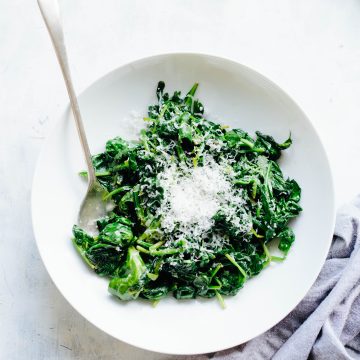 Serving bowl with wilted spinach topped with butter and Parmesan.