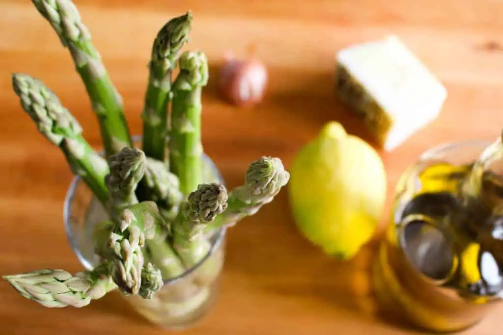 Top view of asparagus spears in a glass next to a whole lemon and shallot.