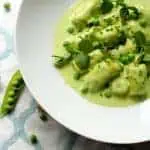 Top view of sweet pea gnocchi with tarragon pea cream in a white bowl.