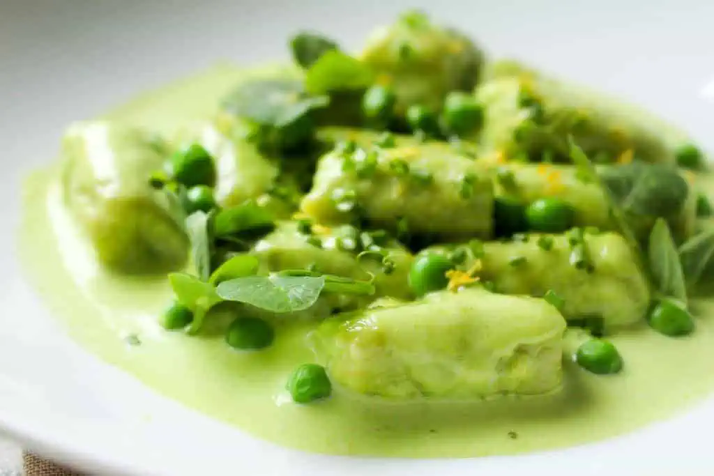 A shallow white bowl with a serving of sweet pea gnocchi with pea cream sauce.