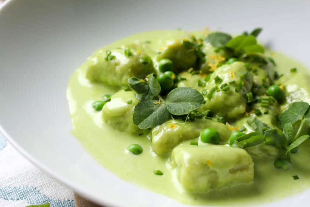 Close up of sweet pea gnocchi and tarragon pea cream sauce in a white bowl.