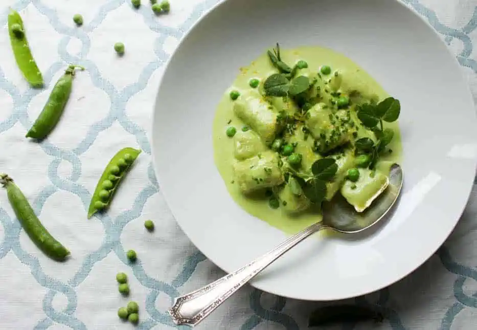 Top view of a shallow white bowl with sweet pea gnocchi in tarragon pea cream.