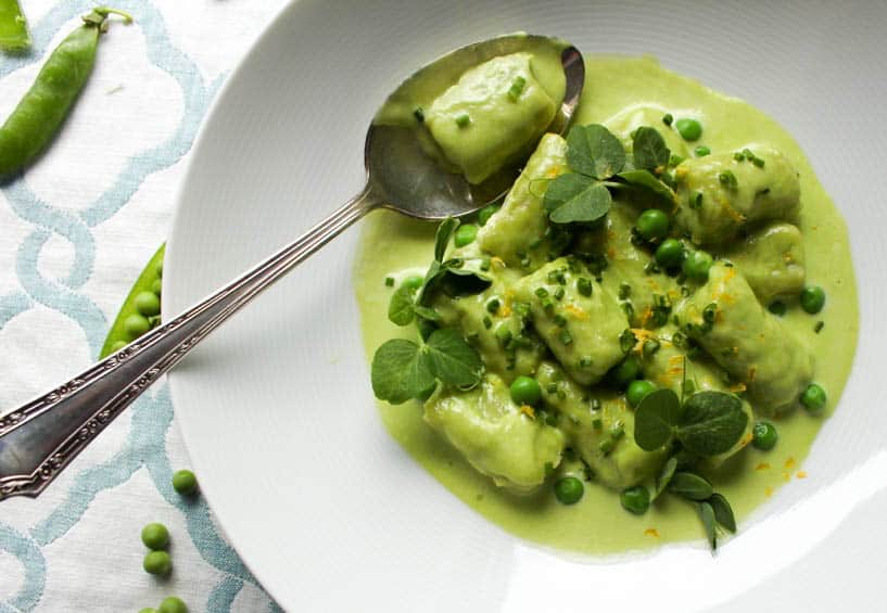A shallow white bowl with a serving of sweet pea gnocchi with pea cream sauce.