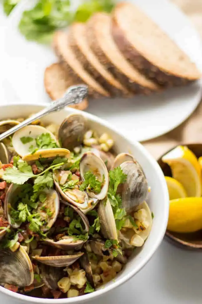 Top view of a bowl of baked clams with a plate of bread slices in the background.
