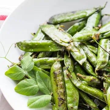 Grilled pea pods in a white bowl.