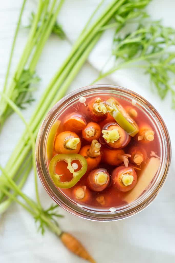 Top view of miniature carrots and sliced peppers in a wide mouth mason jar with pickling liquid.