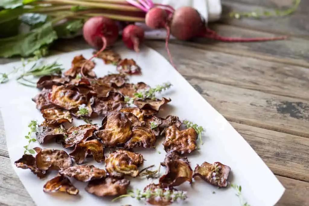 Crispy oven baked beet chips and fresh thyme sprigs on a sheet of white paper.