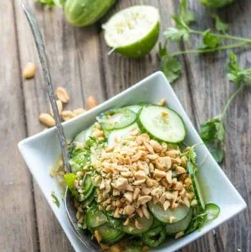 Top view of a square bowl of Thai cucumber salad with a spoon.