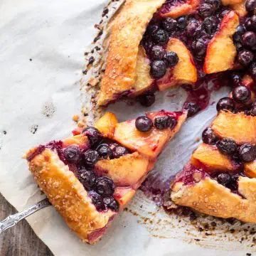 A spatula lifting out a slice of blueberry peach crostata.