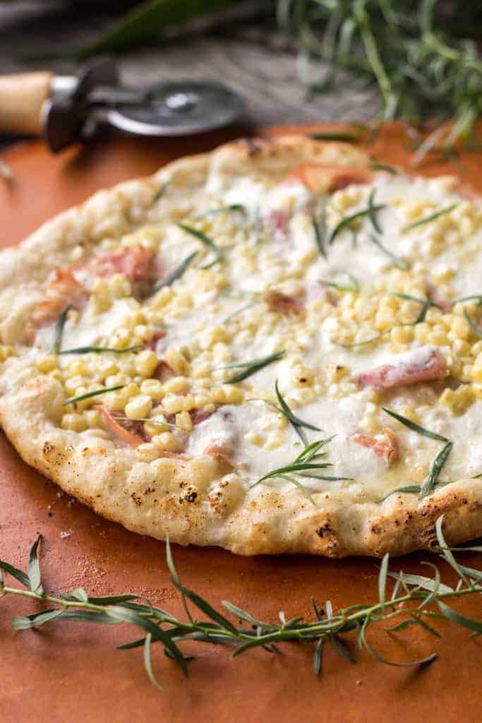 Close up top view of grilled pizza with corn, rosemary, and prosciutto.