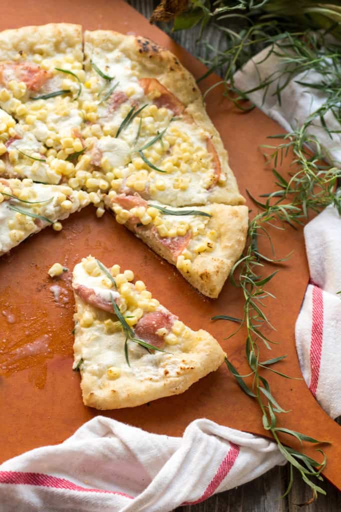 Top view of a prosciutto and corn grilled pizza with fresh rosemary sprigs.