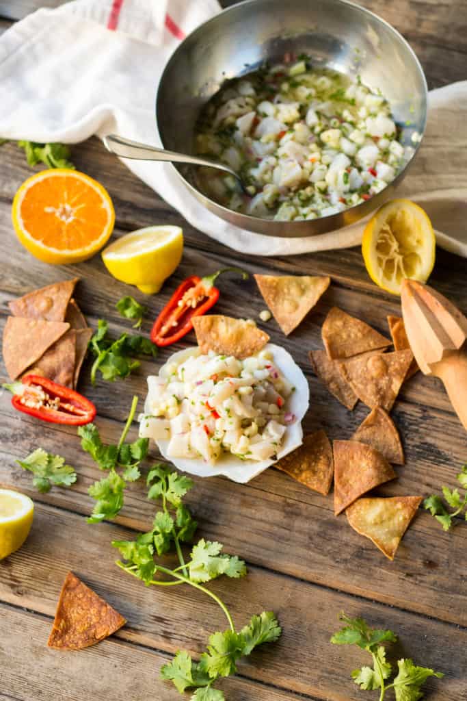 Top view of a wood table set with pita chips, scallop ceviche, and halved lemons and hot peppers.