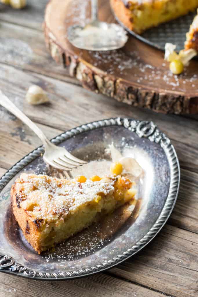 Top view of a triangle slice of husk cherry torte on a silver plate next to a fork,