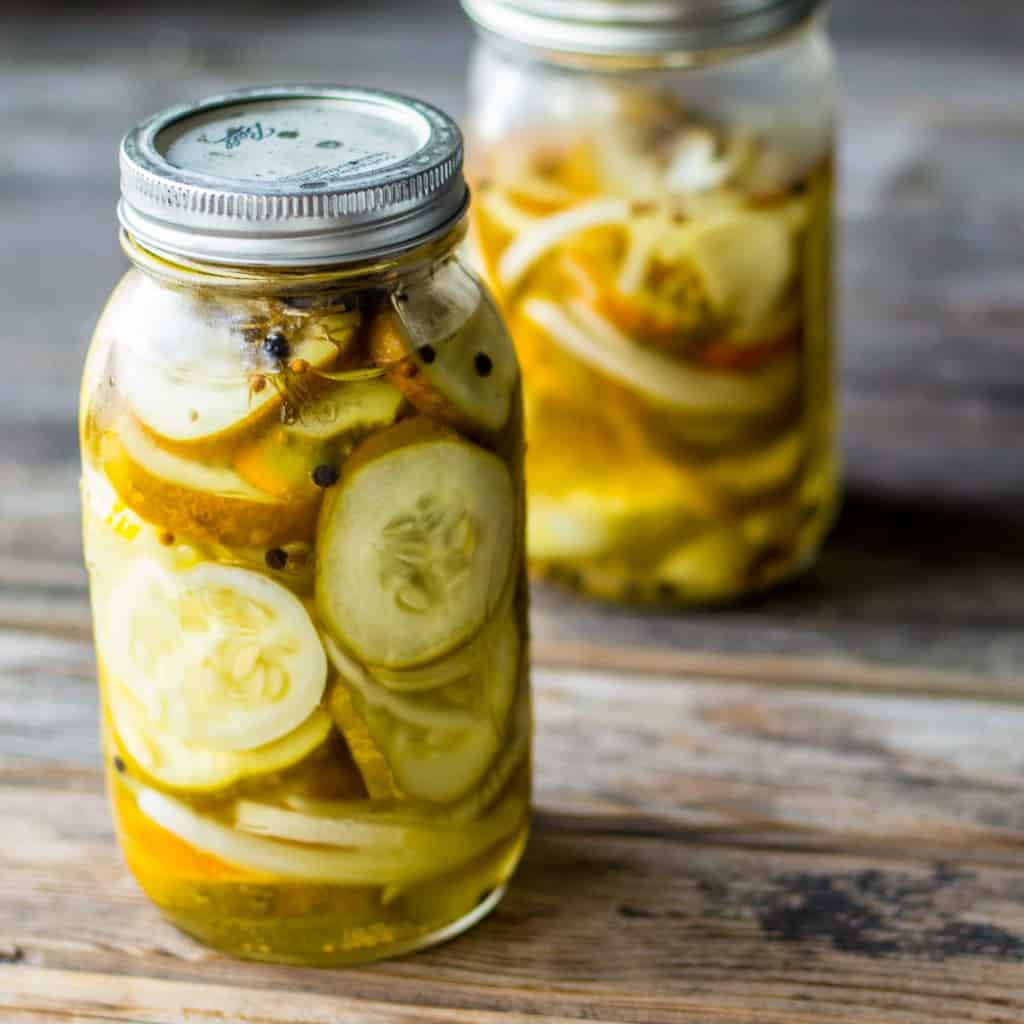 Side view of two half gallon mason jars of dill pickle rounds on a wood table.