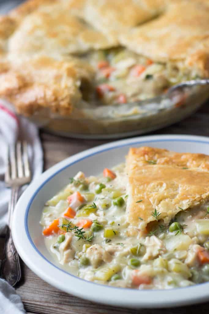 A serving of chicken pot pie on a plate next to the the baking dish.