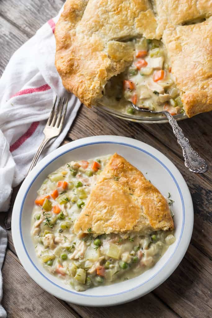 Top view of a baking dish next to a plate with a serving of chicken pot pie.