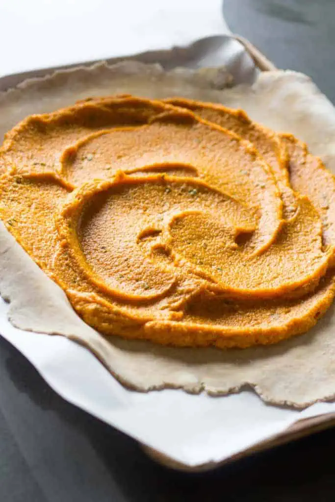Top view of pumpkin puree spread on top of pastry crust on a parchment lined baking sheet.