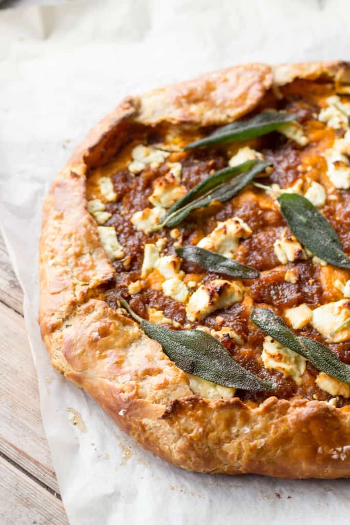 Top view of a pumpkin, goat cheese, and onion galette on parchment paper on a wood table.