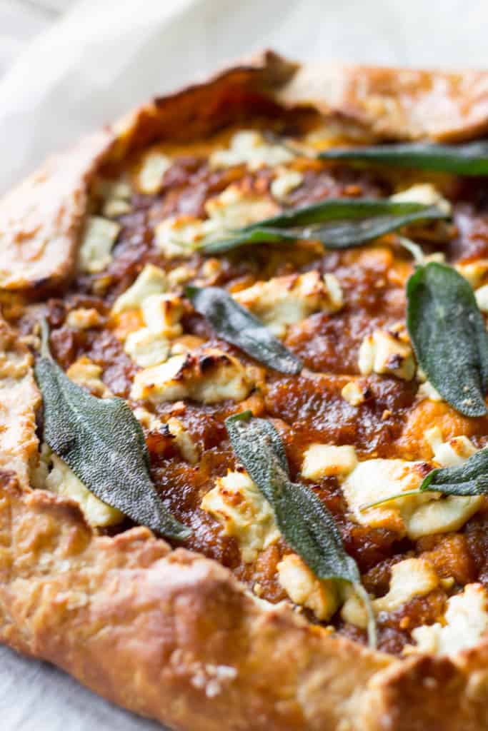 Close up of sage leaves baked into a pumpkin, goat cheese, and onion galette.