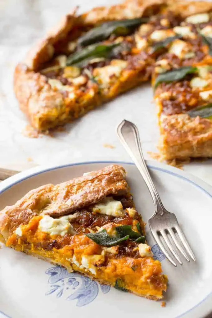 Close up of a slice of pumpkin galette and a fork on a white dinner plate.