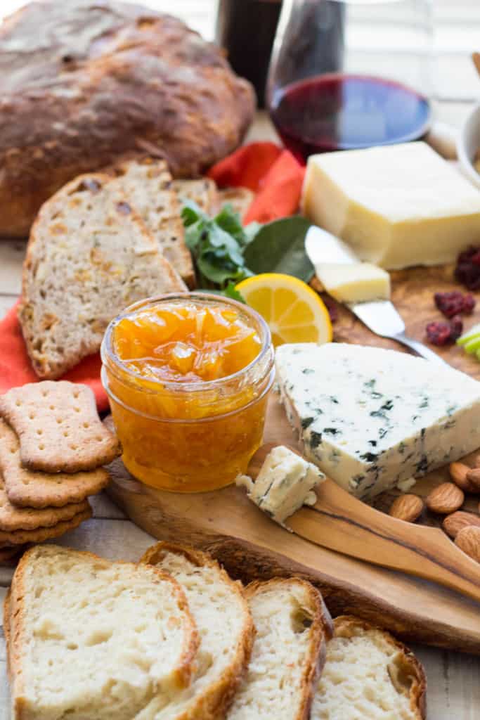 A charcuterie board with several cheeses, crackers, toast points, and a jar of Meyer lemon marmalade.