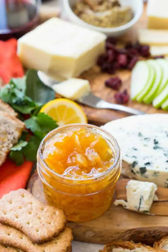 A small mason jar of Meyer lemon marmalade next to cheese and sliced apples on a board.