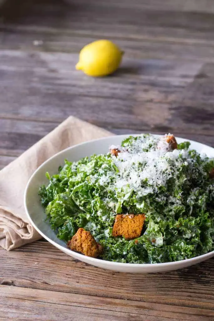White bol of kale salad topped with cheese and croutons.