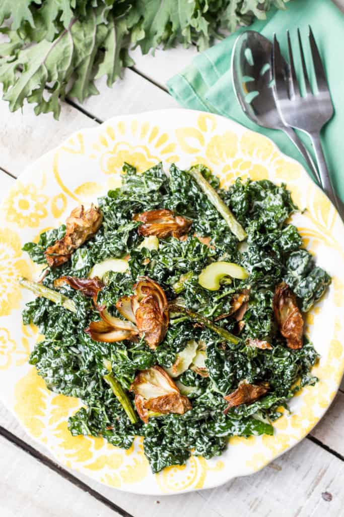 Top view of a yellow dinner plate filled with kale and asparagus salad topped with fried artichoke.