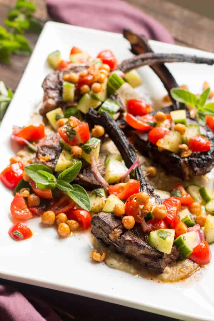 Closeup of lamb chops and chickpea tomato cucumber salad on a white serving platter.