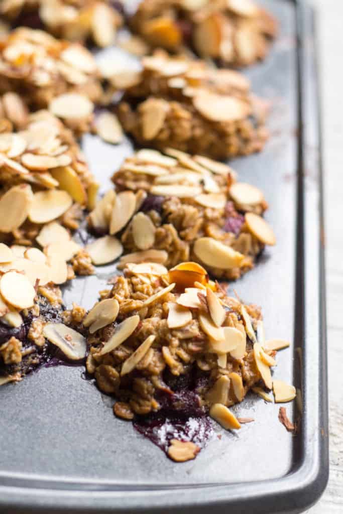 Close up of sliced almonds pressed into the tops of blueberry oatmeal cups in a muffin tin.