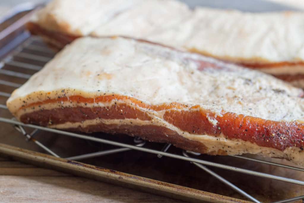 Slabs of homemade bacon curing on a wire rack.