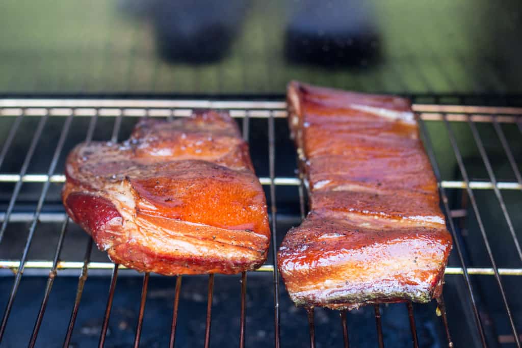 Slabs of homemade bacon on a rack inside a smoker.
