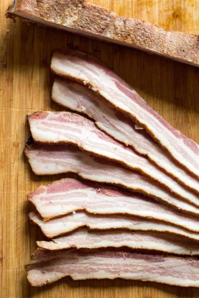 A wooden cutting board with thickly sliced bacon.