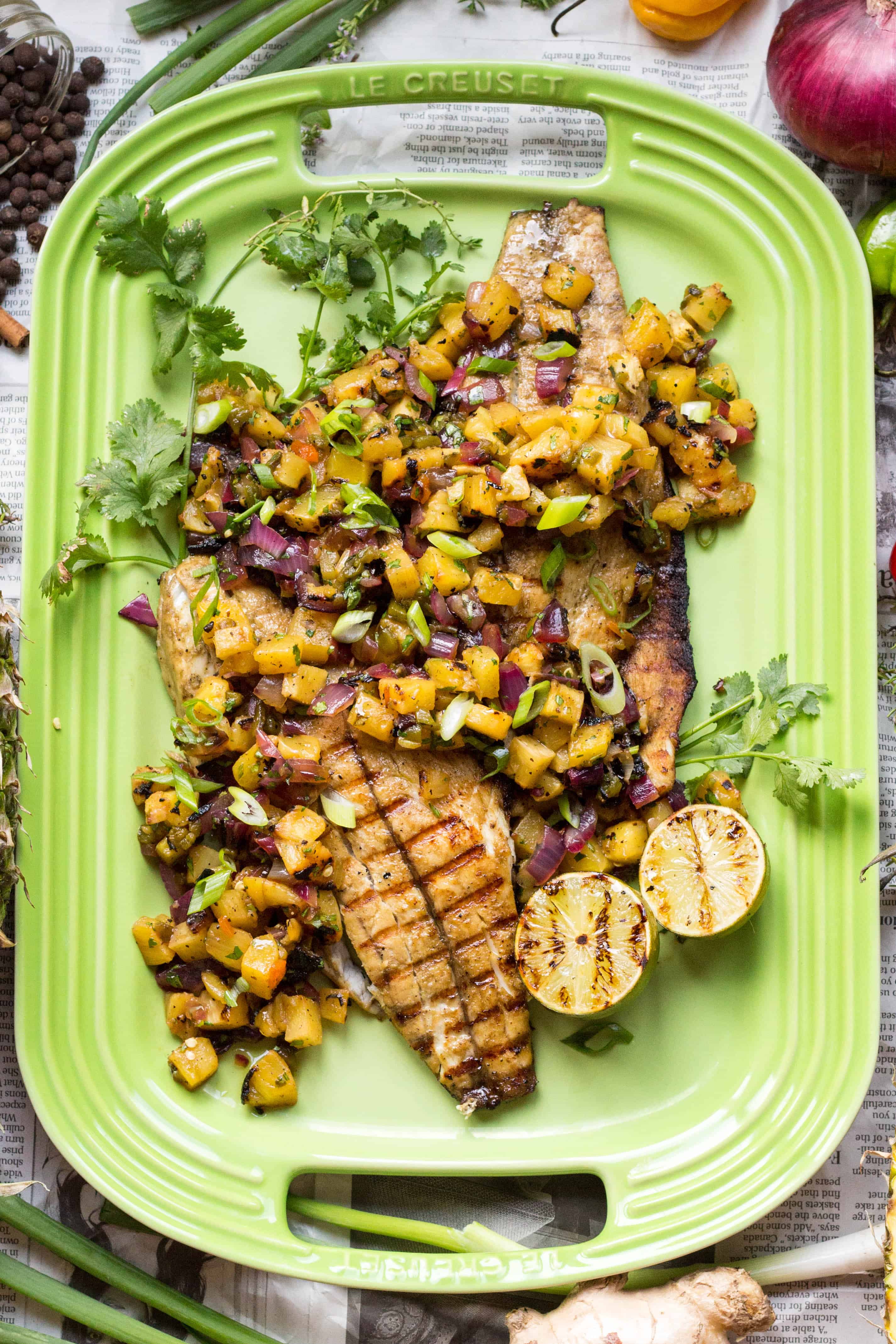 Top view of a green rectangular serving platter with jerk barramundi and pineapple salsa.