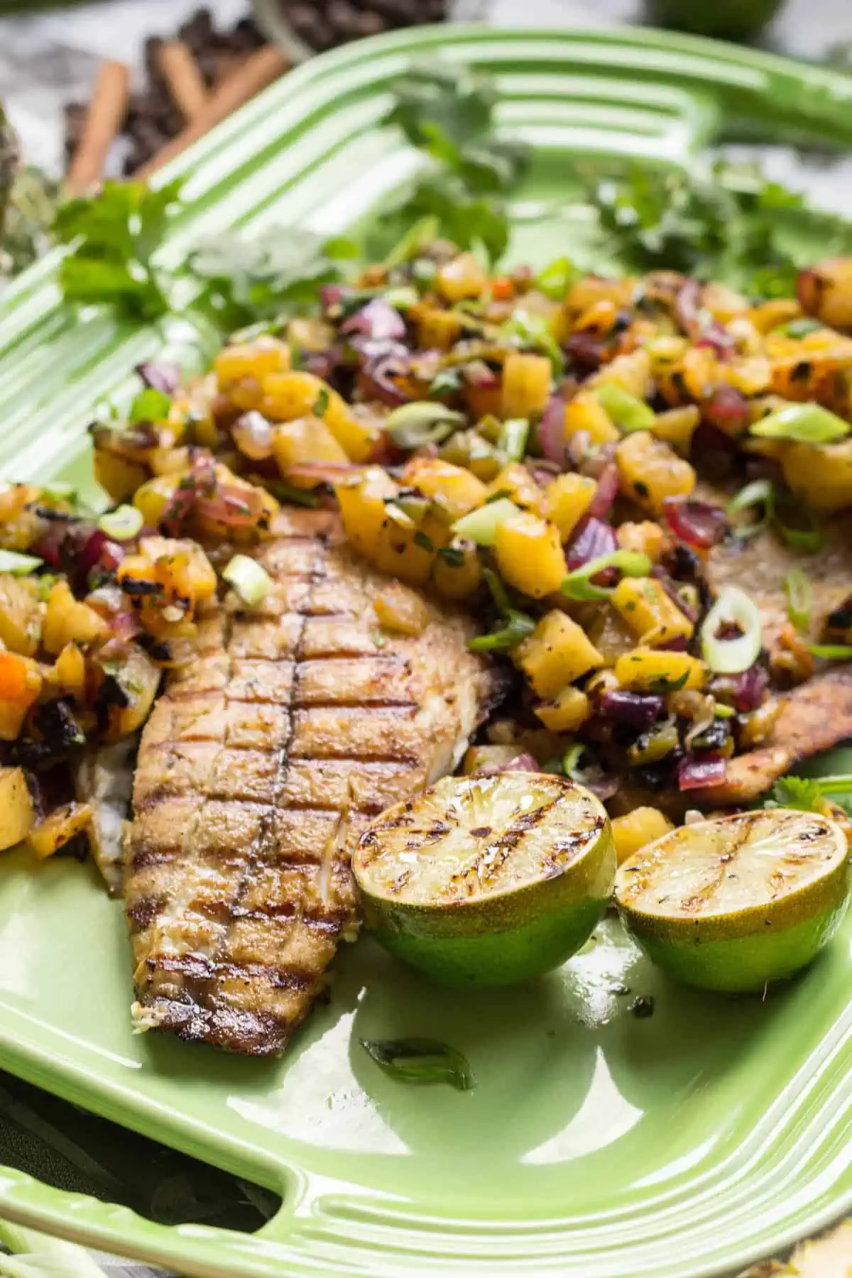 Serving platter with grilled barramundi, lime halves, and fresh pineapple salsa.